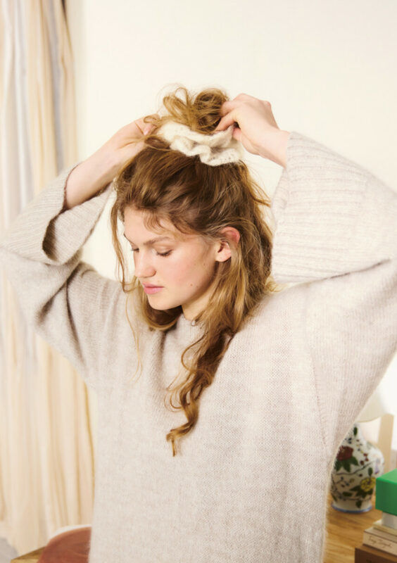 Kvinna som sätter upp sitt hår med en vit scrunchie stickad i Tynn Silk Mohair 1012 Natur i mönster från Sandnes Garn.
