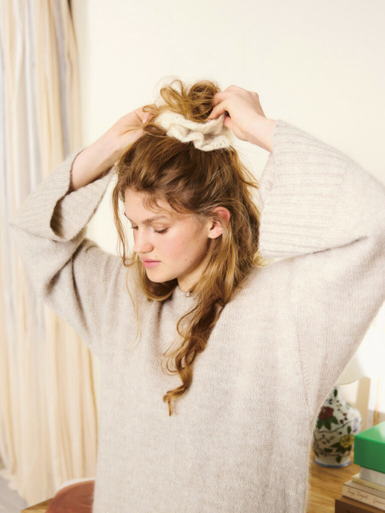 Kvinna som sätter upp sitt hår med en vit scrunchie stickad i Tynn Silk Mohair 1012 Natur i mönster från Sandnes Garn.