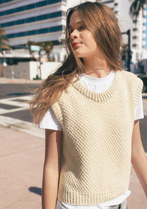 Kvinna utomhus som bär en vit top stickad i Mandarin Petit 1012 Naturvit i mönster Rose Top från Sandnes Garn.