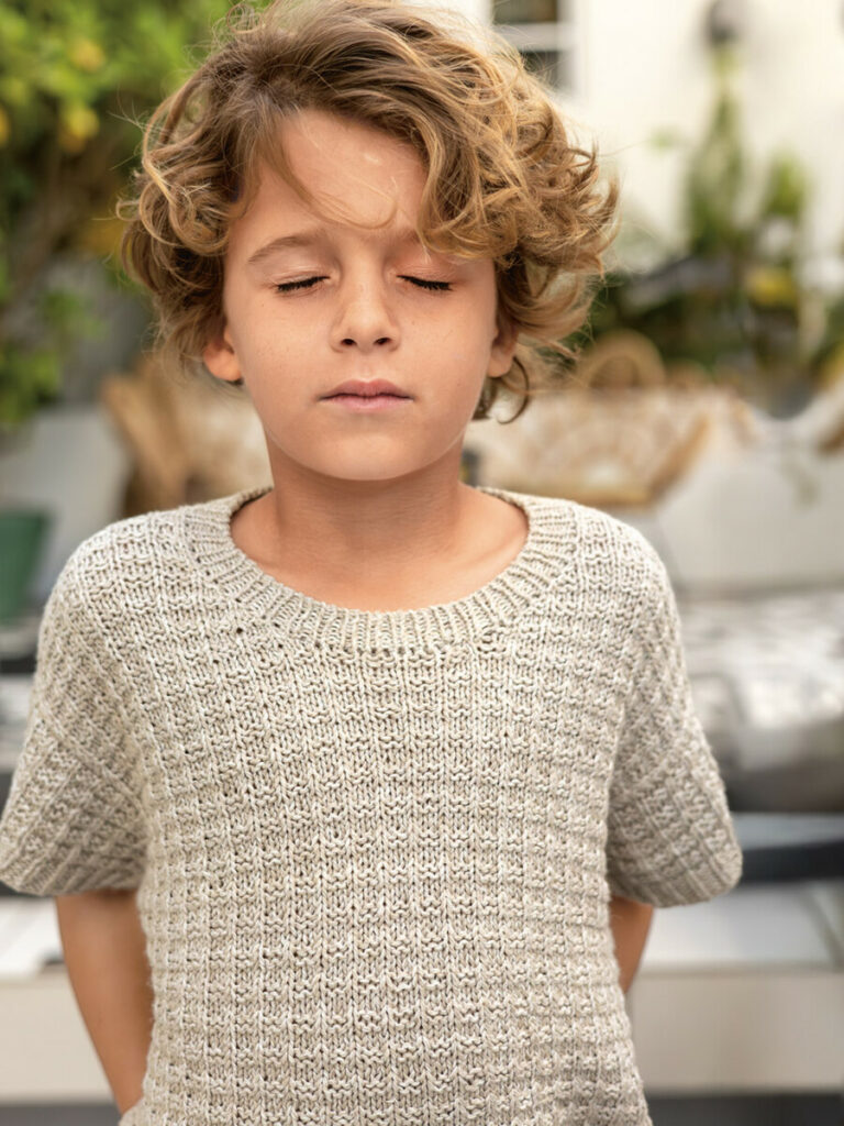 Ung pojke som blundar som bär en grå t-shirt stickad i Line 3820 Pärlgrå i mönster från Sandnes Garn.