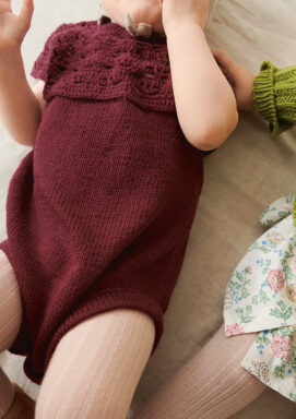 Liten bebis som ligger ner och bär lila Indy Body stickad i Sandnes Mandarin Petit Dyp Burgunder 4372 i mönster för barn från Sandnes Garn.