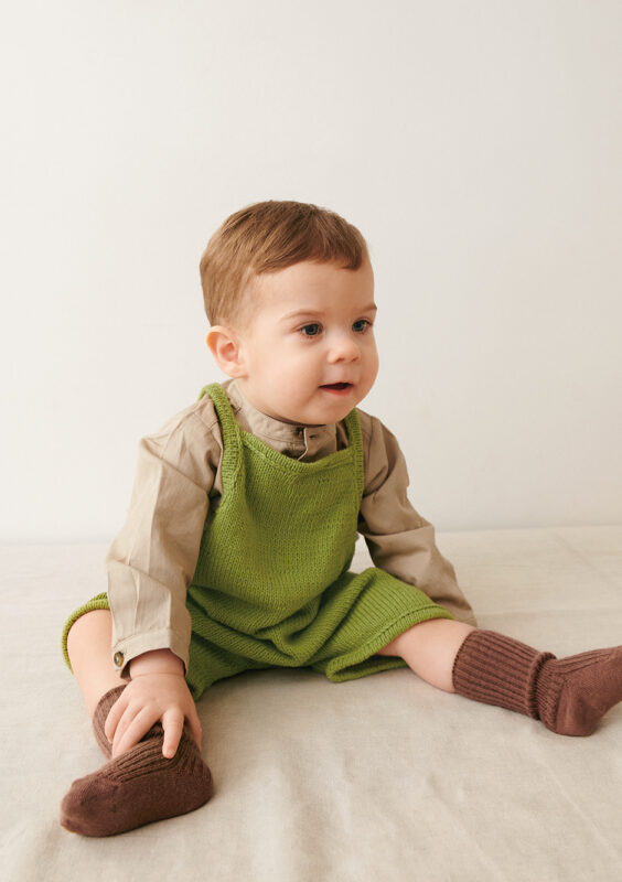 Liten bebis som sitter ner och bär grön Bunny Shorts Baby stickad i Sandnes Mandarin Petit Matcha 9564 i mönster för barn från Sandnes Garn.