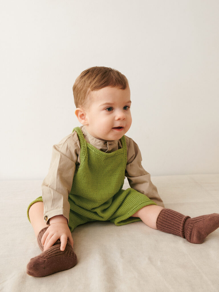 Liten bebis som sitter ner och bär grön Bunny Shorts Baby stickad i Sandnes Mandarin Petit Matcha 9564 i mönster för barn från Sandnes Garn.