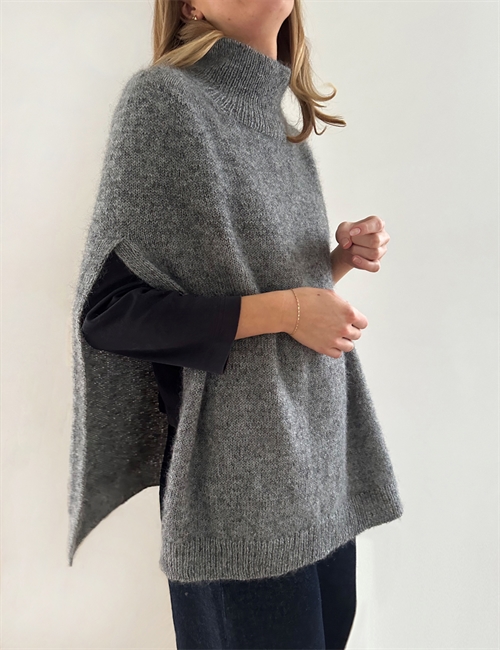Kvinna som bär långärmad svart tröja med grå cape över stickad i mönster Darcy Capy från Le Knit.