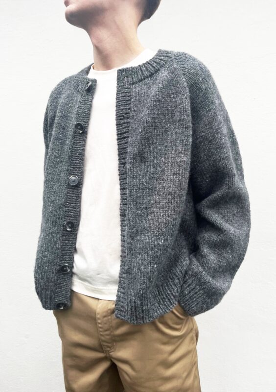 En man som bär vit t-shirt samt grå kofta med grå knappar stickat i mönster Foundation Cardigan Man från Le Knit.
