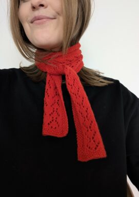 en kvinna har på sig en röd scarf i hålmönster virad runt halsen stickad i garnet sunday från sandnes