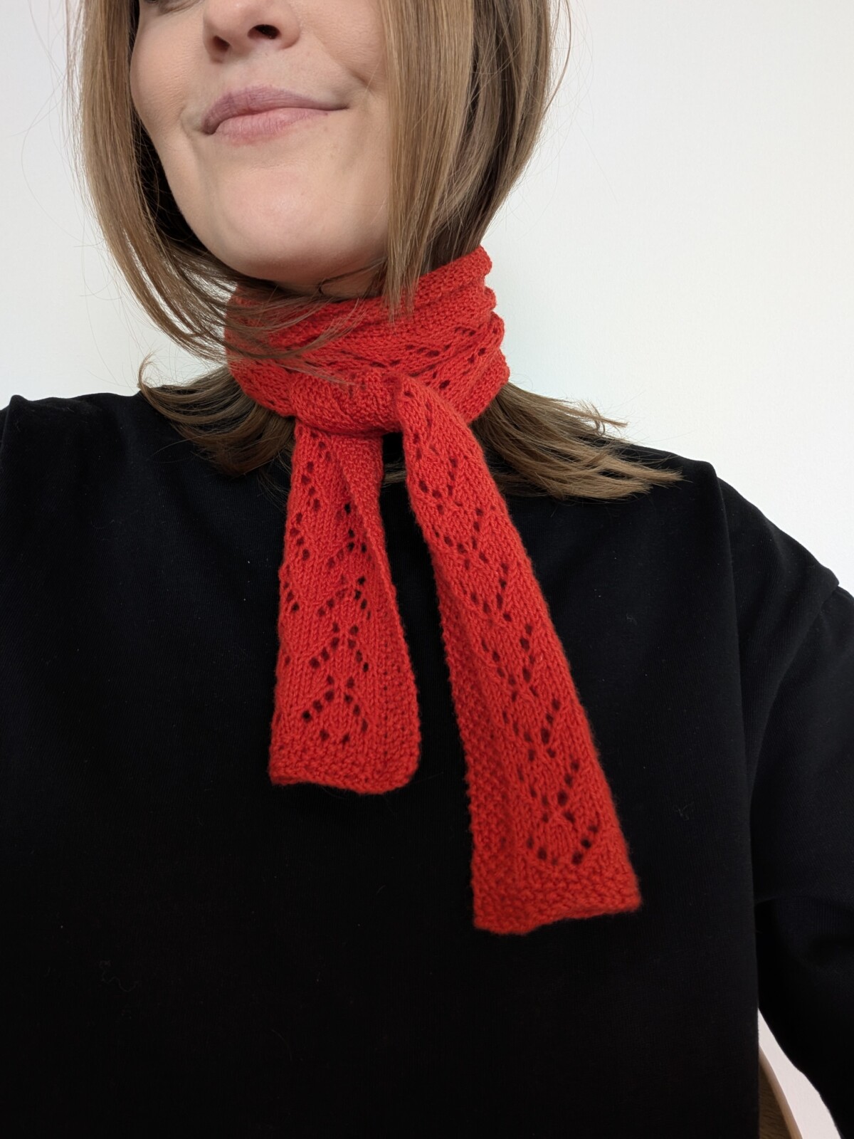 en kvinna har på sig en röd scarf i hålmönster virad runt halsen stickad i garnet sunday från sandnes