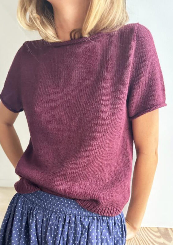Kvinna står med händerna i fickorna och har en t-shirt på sig i burgunder färg