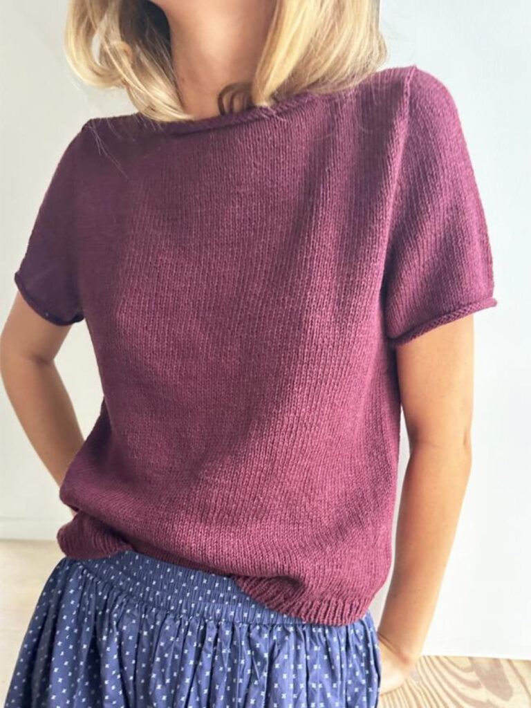 Kvinna står med händerna i fickorna och har en t-shirt på sig i burgunder färg