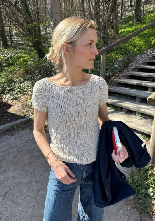 Kvinna står utomhus med vit tröja stickad i mönster Wave Tee från PetiteKnit.
