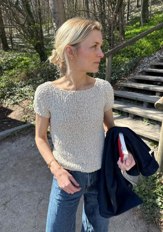 Kvinna står utomhus med vit tröja stickad i mönster Wave Tee från PetiteKnit.