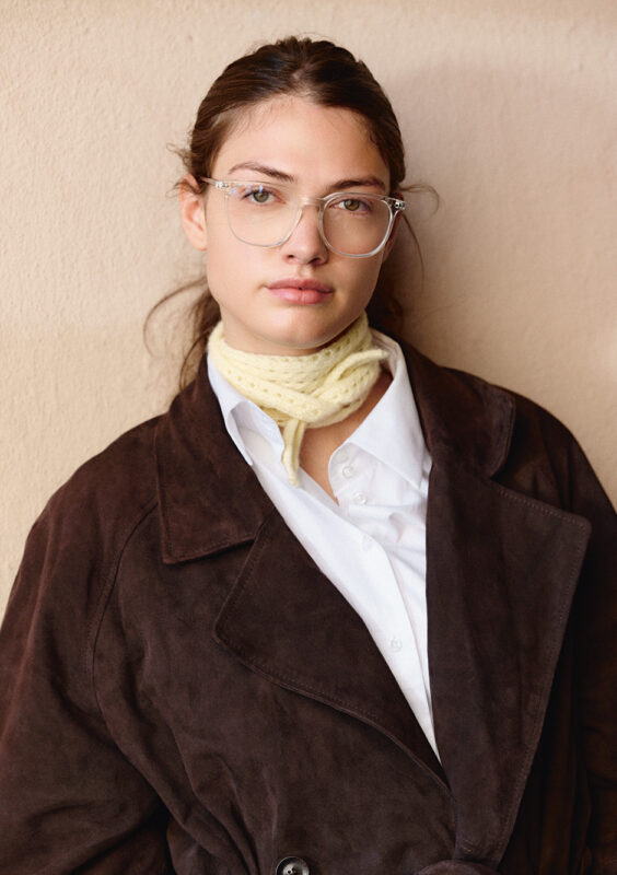 kvinna med mörk rock med vit skjorta under har en ljusgul stickad scarf knutan runt halsen