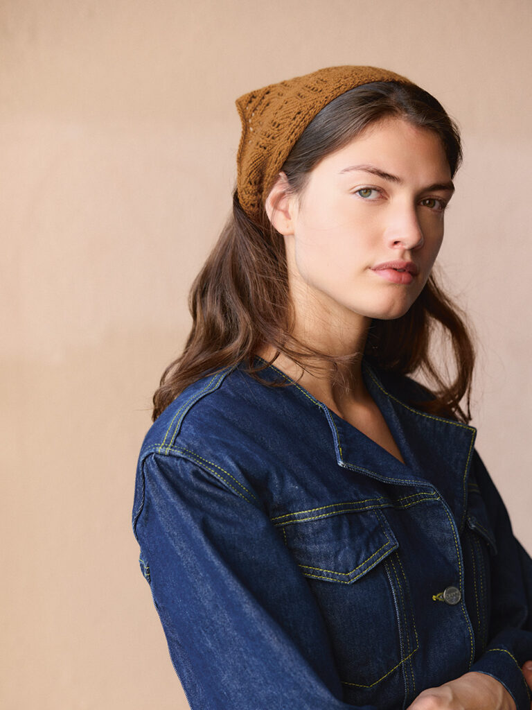 brunhårig kvinna med jeansskjorta har på sig en brunbeige stickad sjalett på huvudet