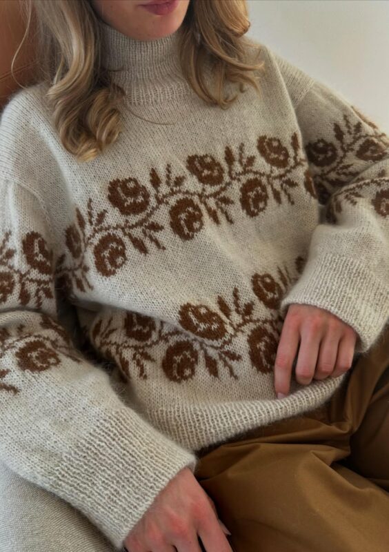 Kvinna som sitter i en fåtölj och bär Rosie Sweater från Le Knit