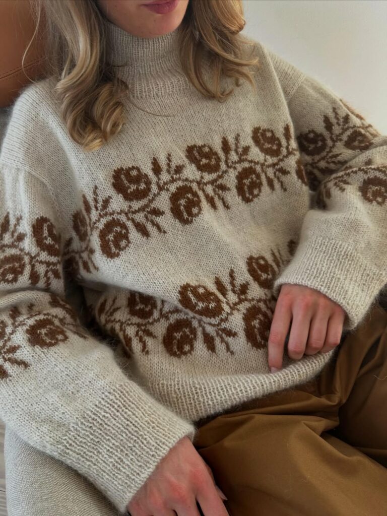Kvinna som sitter i en fåtölj och bär Rosie Sweater från Le Knit