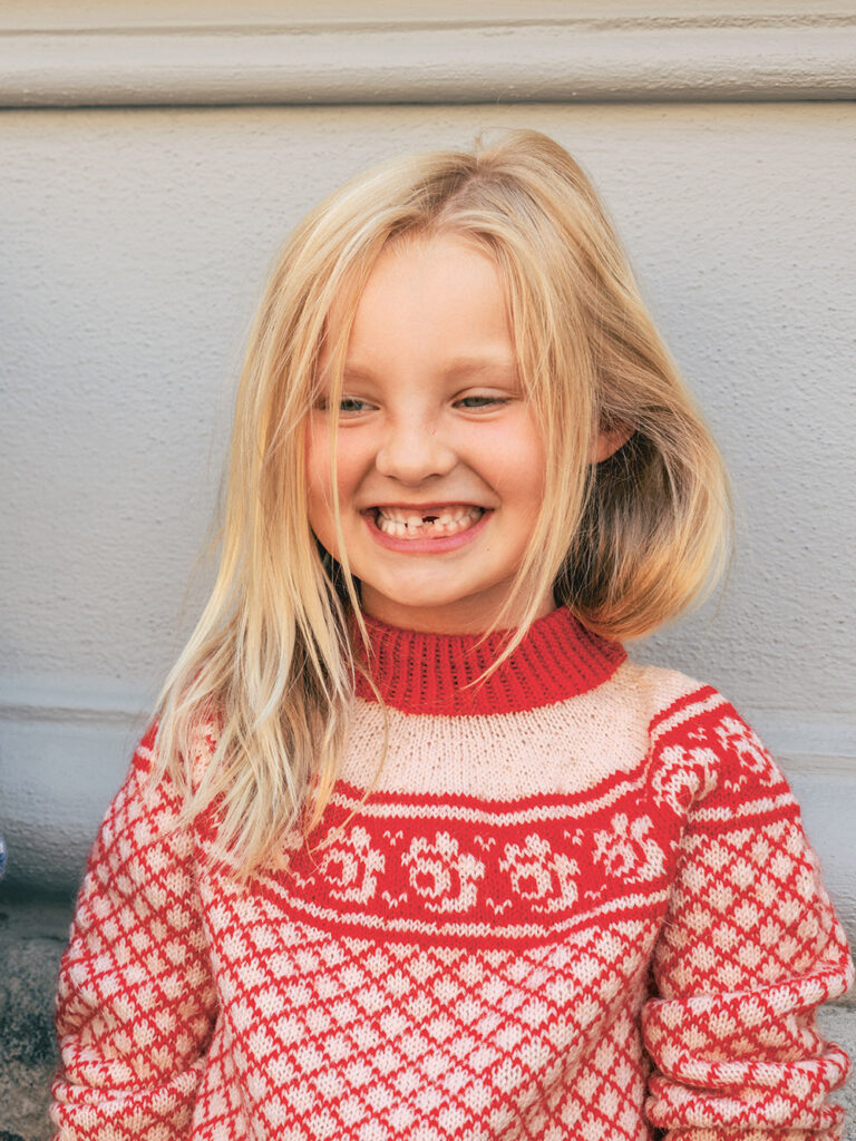 blondhårig flicka med stickad tröja i rött med vita rosor på