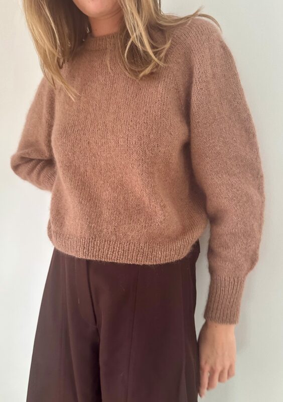 Kvinna som står mot en vägg och har på sig Darcy Blouse från Le Knit