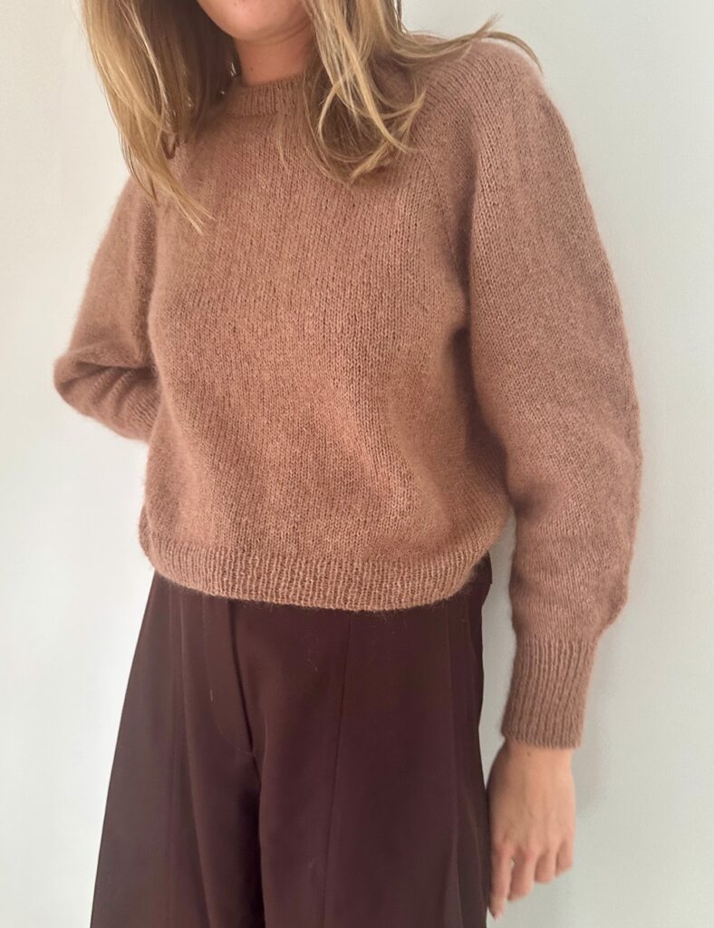 Kvinna som står mot en vägg och har på sig Darcy Blouse från Le Knit