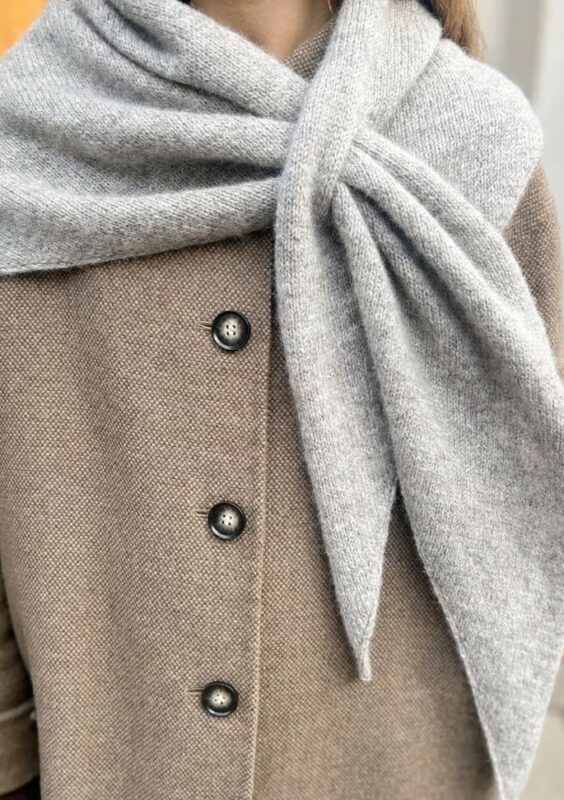 en kvinna med camelbeige kappa har på sig en grå stickad sjal över axlarna